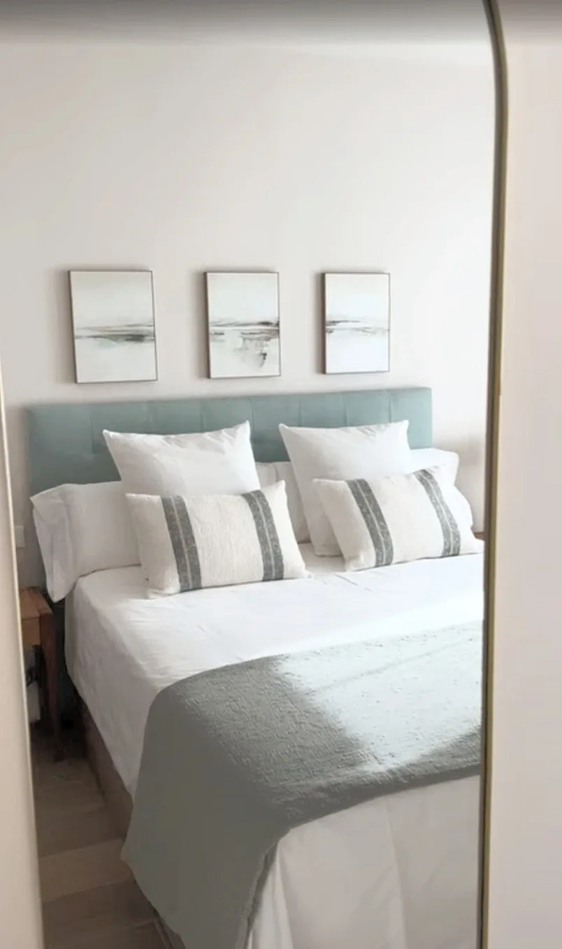 Dormitorio con cabecero verde agua, ropa de cama blanca y trío de cuadros · Ana Uría Interiorismo