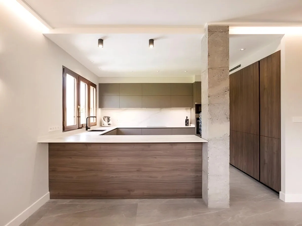 Cocina en península con frentes de madera y encimera blanca · Ana Uría Interiorismo
