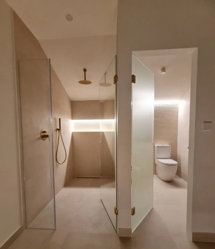 Baño con mampara de vidrio, ducha de obra y grifería dorada · Ana Uría Interiorismo